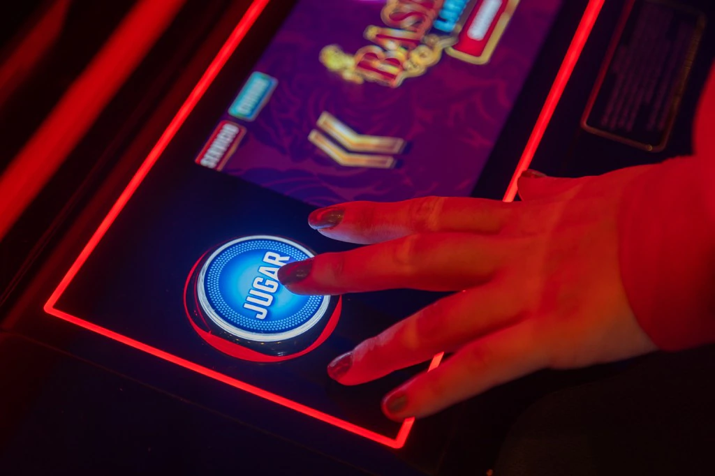 Mano pulsando el botón Jugar de un slot en Casino Arena Maipú